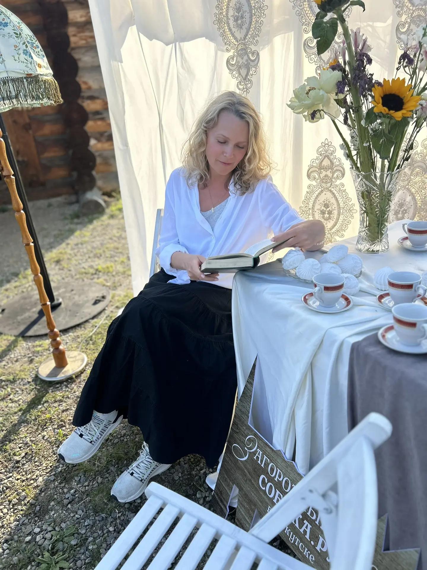Маргарита читает книгу за столом на открытом воздухе